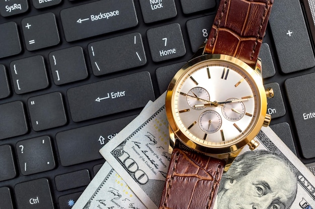 Wrist watch with money on the laptop keyboard Top view