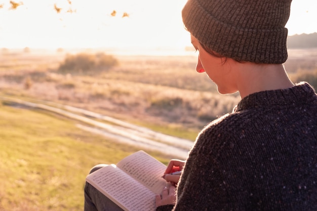 Writing a diary in beautiful nature. Woman facing evening sun takes notes into a notepad