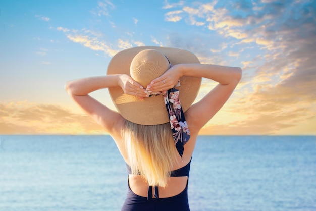 XABeautiful girl in a straw hat on the background of the sky with clouds and the sea Back view