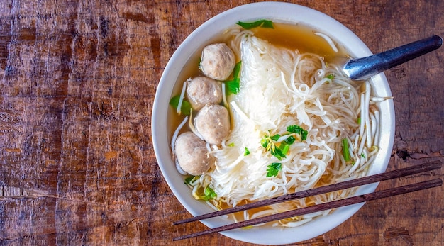 XANoodle and meatballs in a bowl on a wooden table