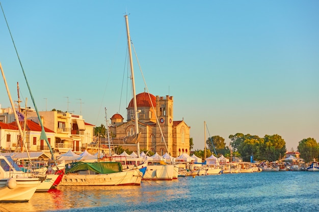 Yachts and waterfront with Ekklisia Isodia Theotokou Church at sunset in Aegina town, Saronic Islands, Greece