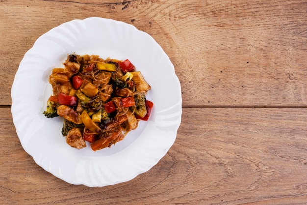 Yakisoba with chicken meat in white dish on wooden table.