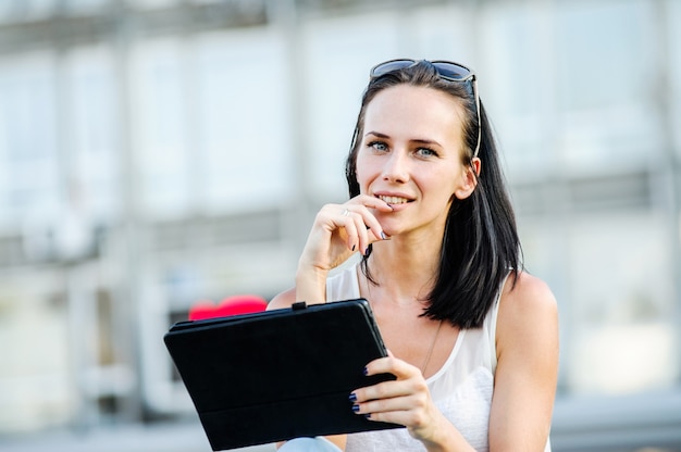 Yang and beautiful modern business woman poses outdoor with tablet computer