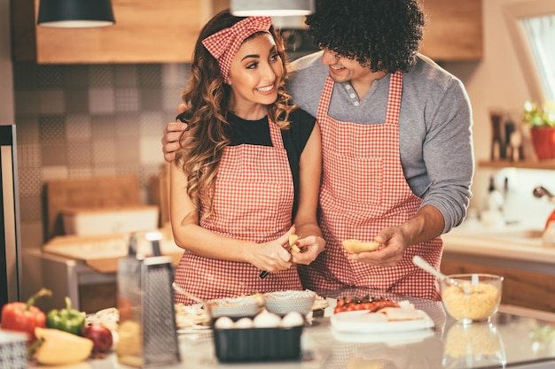 Yang cute couple making pizza in their own kitchen, looking each other with love.