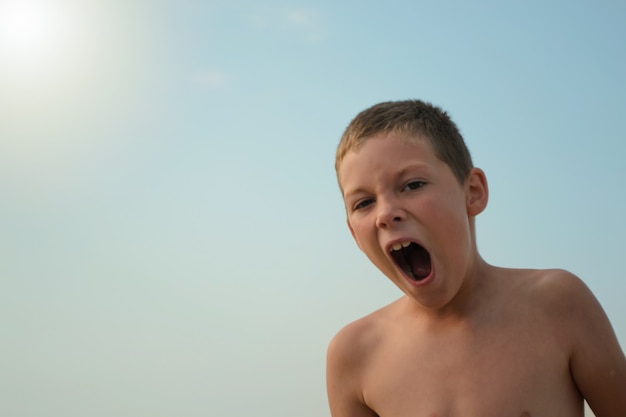 yawning boy against the blue sky on a sunny day.