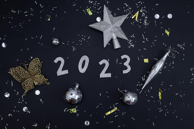 Year 2023 festive flatlay arrange with sparkling golden and silver ornaments on black background