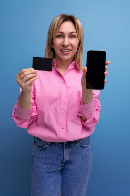 A year old blond woman with shoulder length hair dressed in a fashionable pink shirt holds a credit