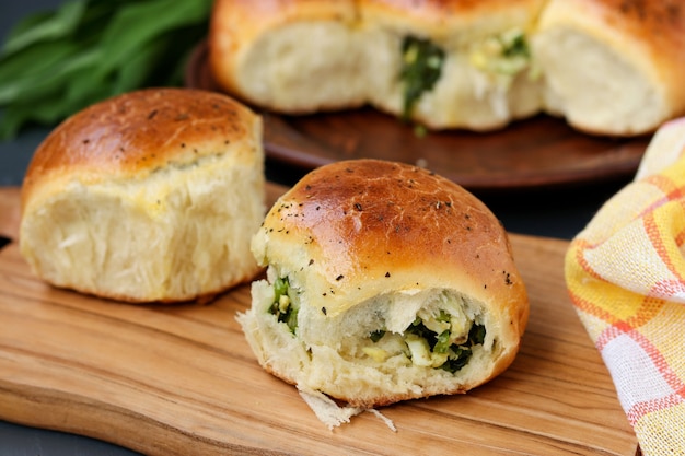 Yeast buns filled with greens and boiled eggs are located on a wooden board against a dark background