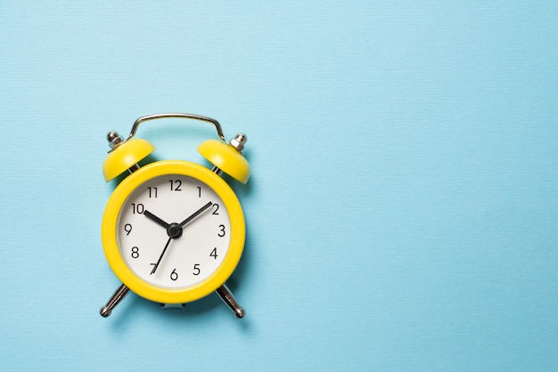 Yellow alarm clock on a blue background. Copy space. Time concept.