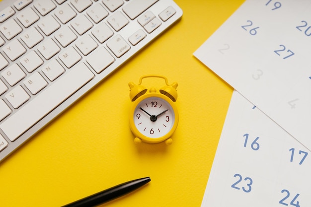 Yellow alarm clock keyboard and calendar on a yellow background closeup Deadline concept