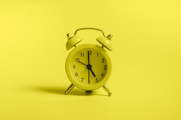 Yellow alarm clock with graduation cap on blue background close up with copy space