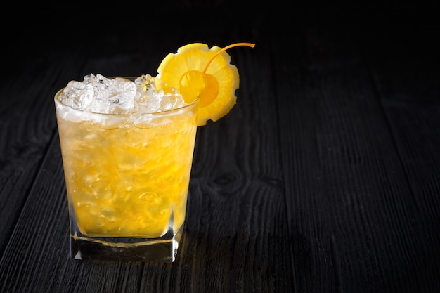 Yellow alcohol cocktail with cherry and lemon on black background