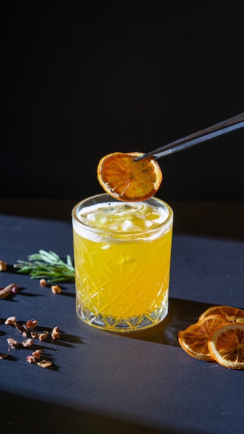 Yellow aperitif cocktail in glass with ice on black background