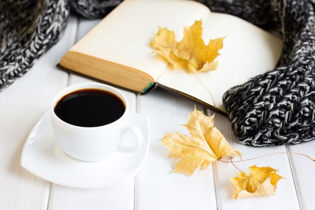 Yellow autumn leaves coffee cup warm knitted scarf with opened old book on wooden boards