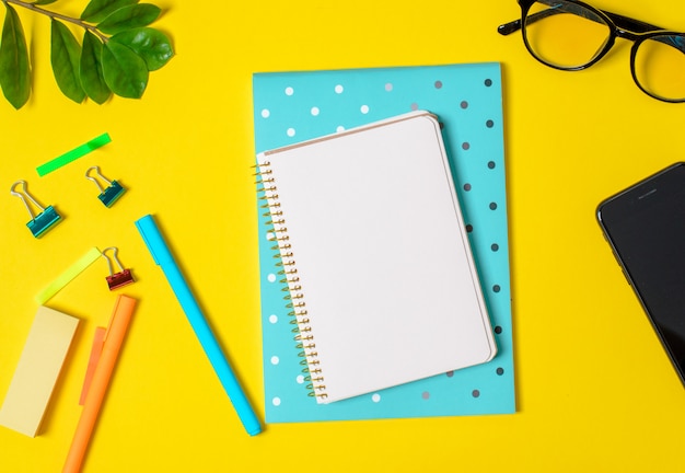 Yellow background, white notebook for records, phone, computer glasses, twig plants, pens, pencils.