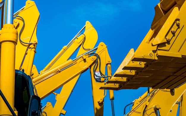 Photo yellow backhoe with hydraulic piston arm against clear blue sky.