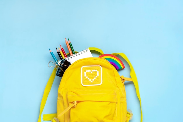 Yellow backpack with school supplies notebook pens eraser numbers isolated on blue background