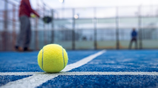 Yellow ball on floor behind paddle net in blue court outdoors Man who playing padel tennis Caucasian player sportsman hitting balls Racquet sport game concept