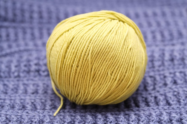 A yellow ball of wool lies on a blue woolen tablecloth. High quality photo