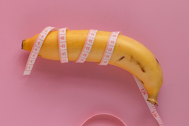 Yellow banana wrapped in measure tape Men penis size concept isolated on pink background