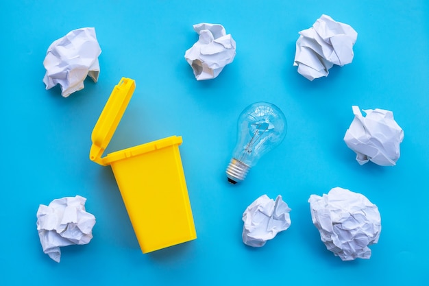 Yellow bin with light bulb and white crumpled paper on blue