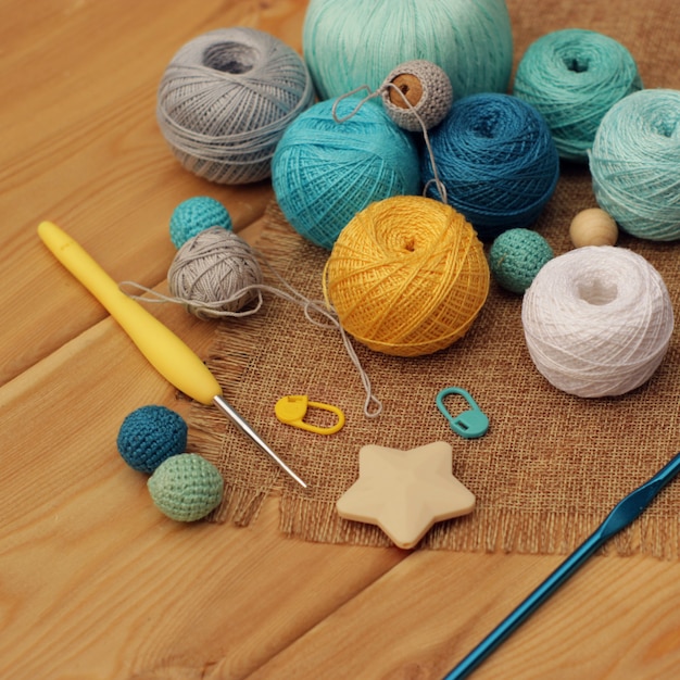 Yellow and blue crochet hooks and balls of cotton thread on a wooden table, copy space.