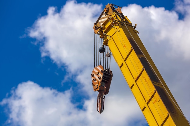 Yellow boom of a loading crane against a blue sky with clouds