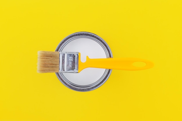 Yellow brush on an open can with white paint on a yellow background closeup top view