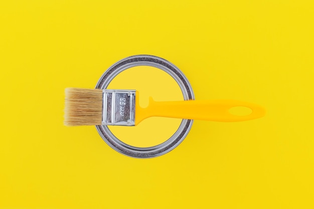 Yellow brush on an open can with yellow paint on a yellow background closeup top view