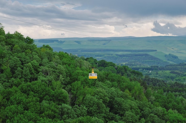 Yellow cabin of the cable car above the forest Funicular cabin over the green hills