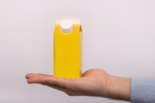 Yellow carton of milk or juice on mans palm on white background