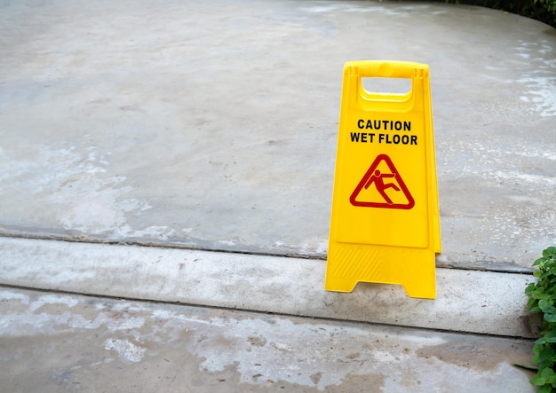 Yellow caution slippery wet floor sign with slippery person warning icon on wet concrete floor background after raining with copy space