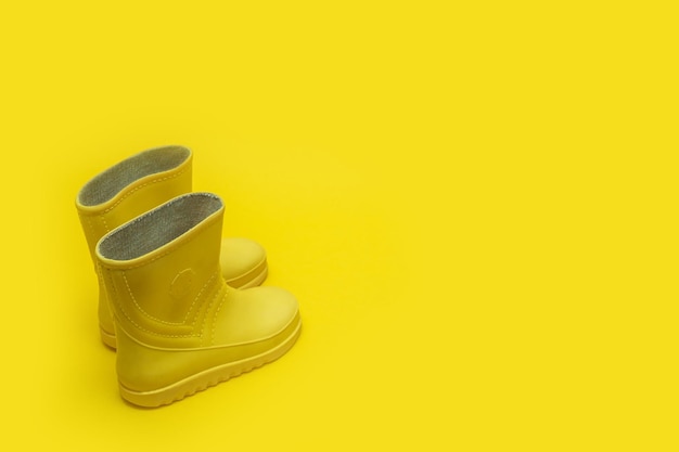 Yellow children's rubber boots on a yellow background with copy space