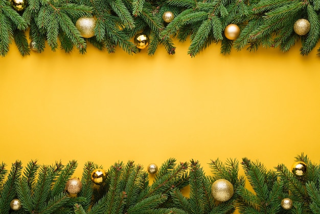 Yellow Christmas or New Year background. Decorative border of fir branches and Christmas balls. Copy space for text