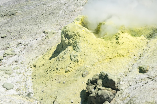 Yellow cone of crystallized sulfur around a smoking solfatara on the slope of a volcano