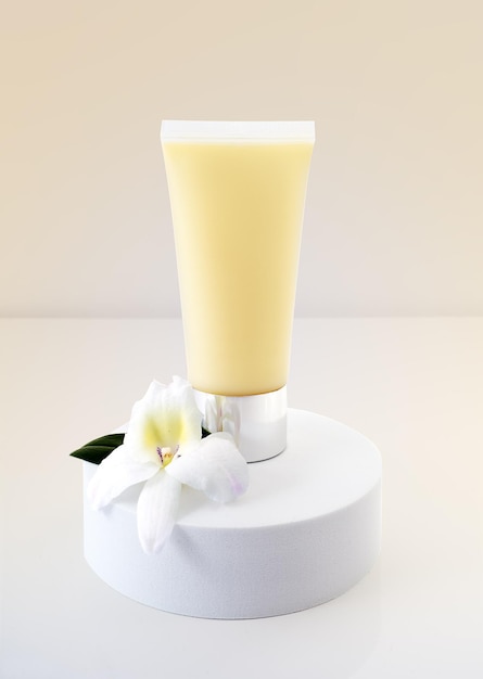 Yellow cosmetic tube light pastel color background orchid flower and green leaf on white podium