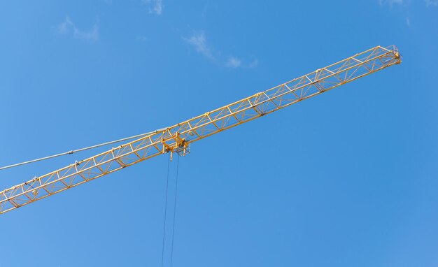 A yellow crane against a blue sky with a cloud in the background.