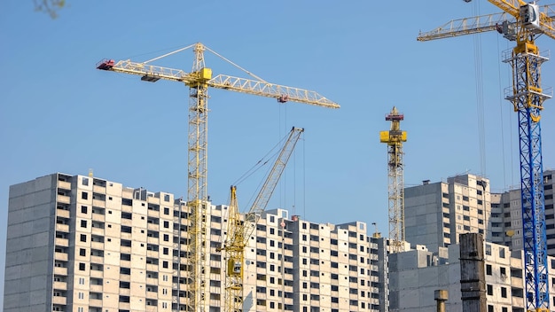 Yellow cranes and high buildings on blue sky background skyscrappers under construction