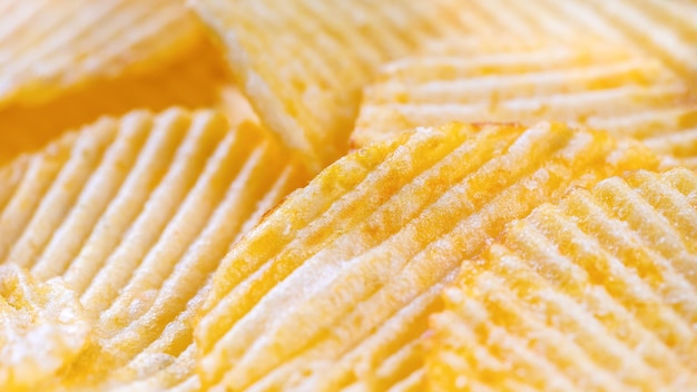 Yellow crispy ridged potato chips close up Food background