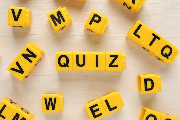 Yellow cubes with word Quiz on white wooden table flat lay