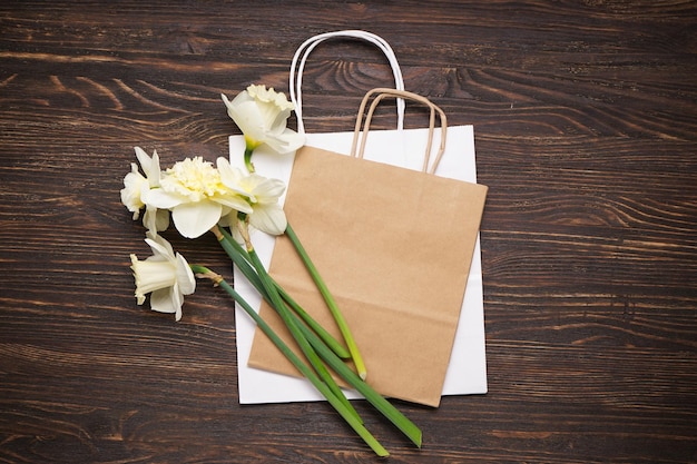 Yellow daffodil flowers and paper bag on wooden background top view