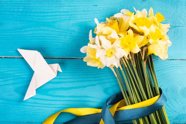 Yellow daffodils with a yellowblue ribbon on a wooden background and a white paper's dove Concept of Peace in Ukraine