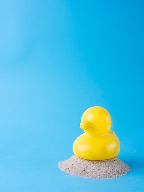 Yellow duck on beach sand, isolated on blue background