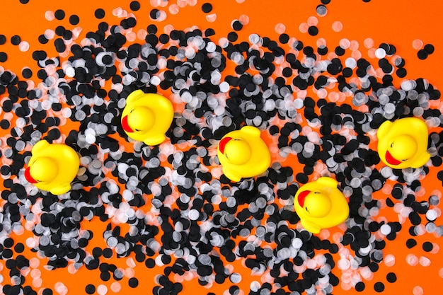 Yellow ducks swim among white black confetti halloween decorations orange background halloween conce...