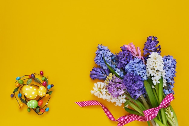 Yellow Easter background. Spring flowers and decorative Easter eggs. Copy space, top view. Easter celebration concept.