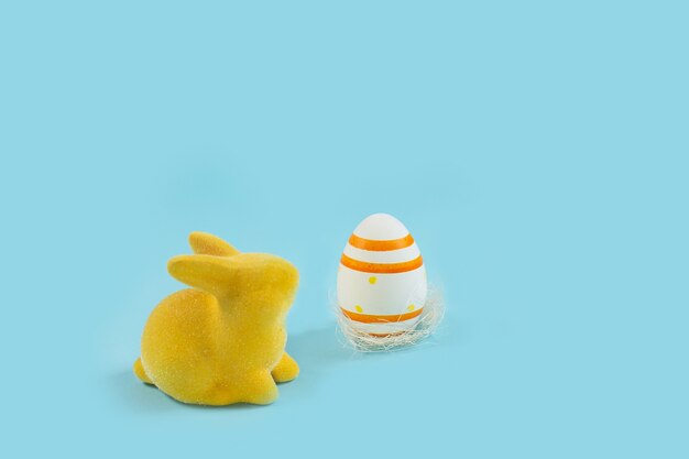 Yellow easter bunny rabbit with painted egg on blue background