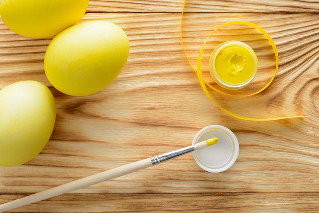 Yellow eggs with a brush and paints on a wooden table.