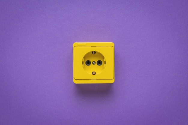 Yellow electrical outlet on a purple background. Stylish design. The place where electrical appliances are connected.