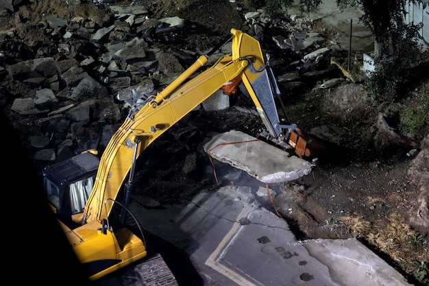 Yellow excavator digger working at night on the street