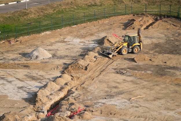 Yellow excavator digging trenches for cables and wires at a construction site